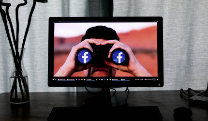 ordinateur allumé sur une image avec une personne ayant des jumelles affichant les logos Facebook sur leurs verres